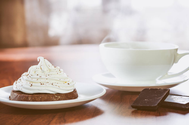 Dort s bílou smetanou, dva kousky čokolády a šálek horké kávy na dřevěný stůl na pozadí - Fotografie, Obrázek
