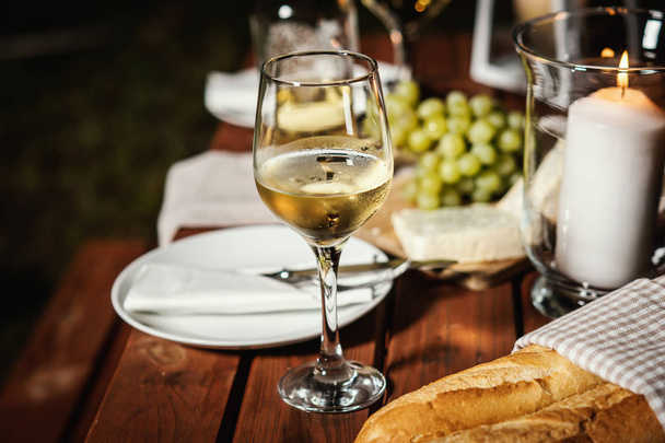cena romantica con un bicchiere di vino, una baguette e spuntini su un vecchio tavolo di legno in una serata estiva
 - Foto, immagini