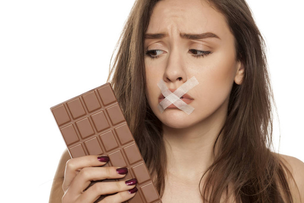 Young woman craving for chocolate with taped mouth on a white background - Φωτογραφία, εικόνα