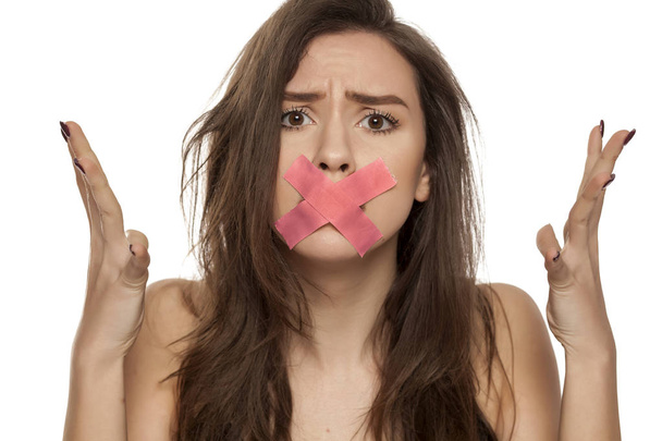 Jovem mulher nervosa com fita adesiva sobre a boca em um fundo branco
 - Foto, Imagem