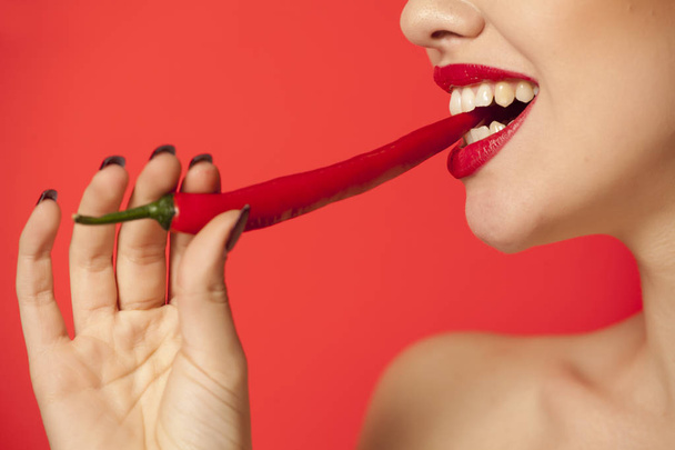 Young sexy woman biting a chili pepper on a red background - Foto, imagen