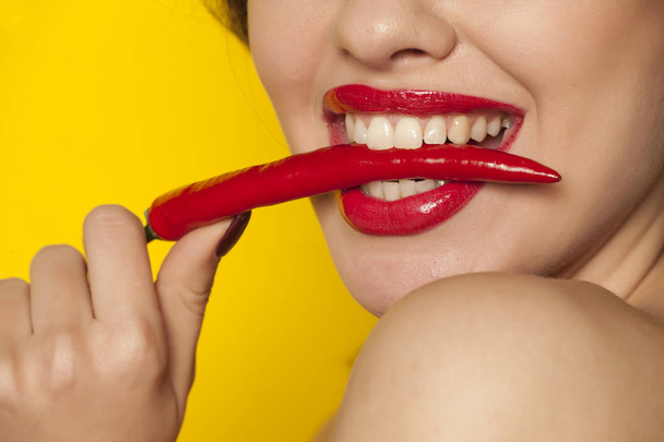 Young sexy woman biting a chili pepper on a yellow background - Foto, Imagen