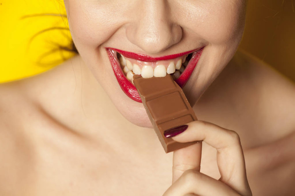Młoda kobieta piękne jedzenie czekolady na żółtym tle - Zdjęcie, obraz