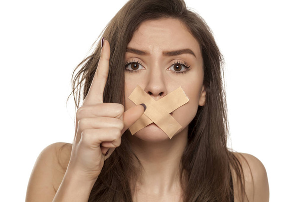 Jeune femme en colère avec du ruban adhésif sur sa bouche sur un fond blanc
 - Photo, image