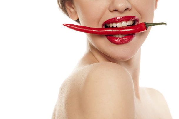 Νέοι σέξι γυναίκα κρατώντας ένα πιπέρι τσίλι με τα δόντια της σε λευκό φόντο - Φωτογραφία, εικόνα