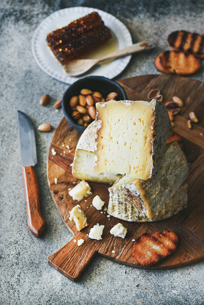 Cheese platter with cheese assortment, nuts, honey and bread on rustic wooden board over grey concrete background - Zdjęcie, obraz