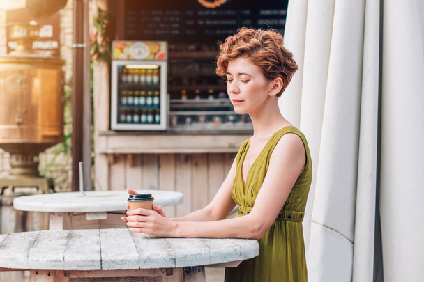 A young woman in a dress drinking coffee in a summer cafe. Pretty woman with cup of coffee. - Foto, afbeelding