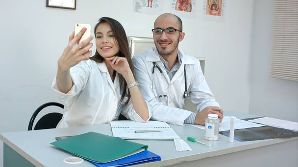 Young doctor and pretty nurse taking selfies on the phone at their desk - Fotó, kép