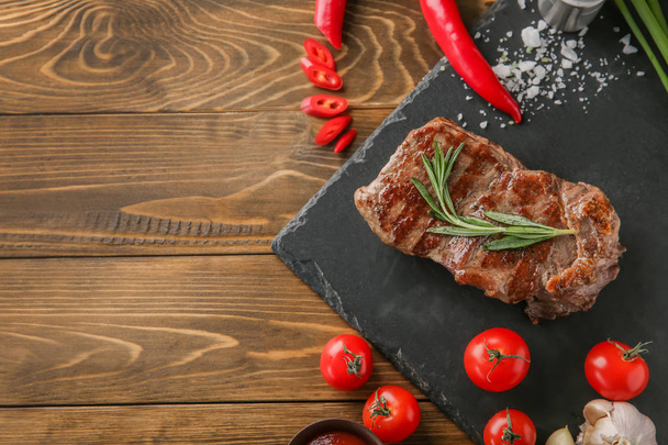 Assiette d'ardoise avec un délicieux steak grillé et légumes sur la table
 - Photo, image