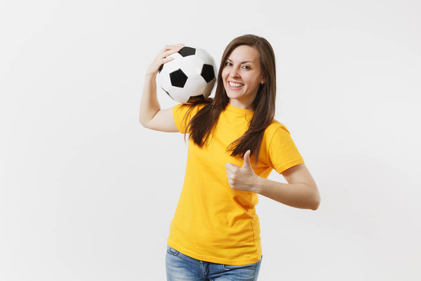 lächelnde junge Frau, Fußballfan in gelber Uniform, der einen Fußballball in der Hand hält und mit erhobenem Daumen auf weißem Hintergrund gestikuliert. Sport, Fußball spielen, jubeln, Fans Menschen Lifestylekonzept - Foto, Bild