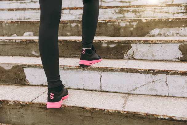 Cropped photo close up of female legs in sportswear, black and pink woman sneakers doing sport exercises, climbing on stairs outdoors. Fitness, healthy lifestyle concept. Copy space for advertisement - 写真・画像