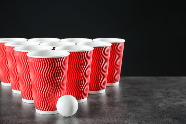 Tazze e palla per birra pong sul tavolo contro sfondo scuro
 - Foto, immagini