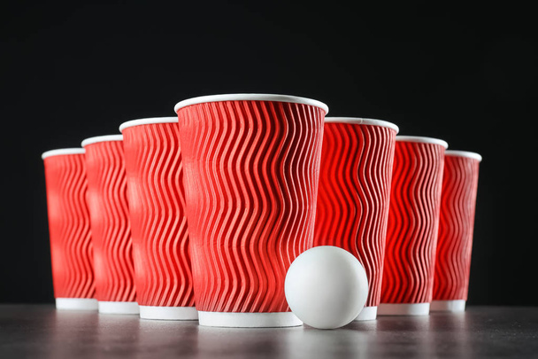 Copas y pelota para pong de cerveza en la mesa sobre fondo oscuro
 - Foto, Imagen