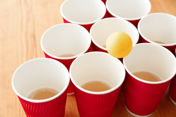 Bekers en bal voor bier pong op houten tafel - Foto, afbeelding