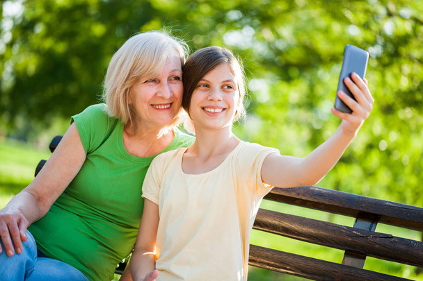 Oma en kleindochter zijn zit in het park en het nemen van de selfie. - Foto, afbeelding