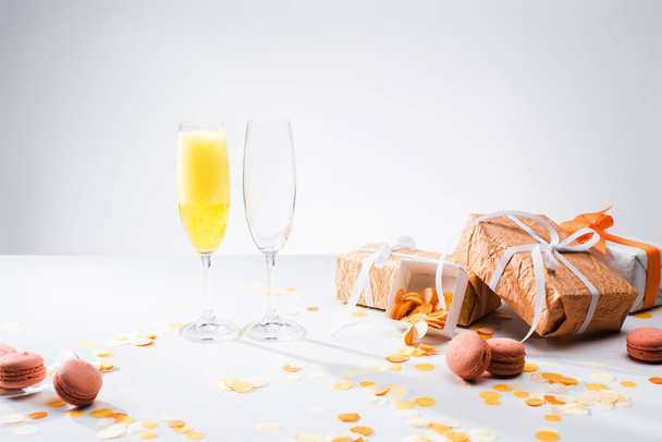 close up view of glassware with yellow champagne, macarons and arranged gifts on grey backdrop - Fotoğraf, Görsel