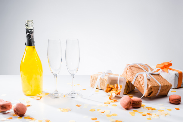 Zamknij widok butelki szampana żółty, puste kieliszki, Makaronki i ułożone prezenty na szarym tle - Zdjęcie, obraz