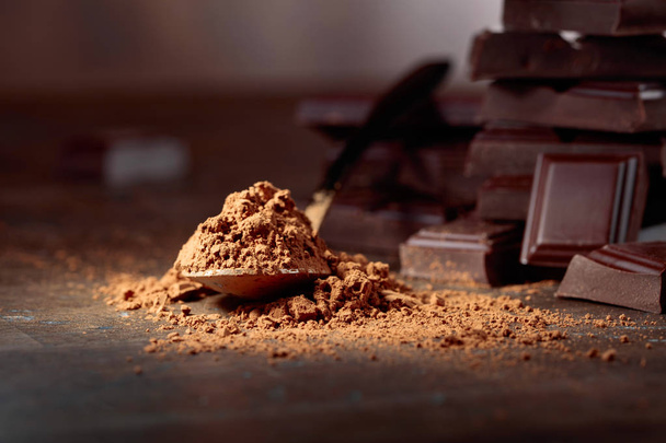 Pedaços de chocolate quebrados e cacau em pó em pequenas colheres em um fundo de madeira
. - Foto, Imagem
