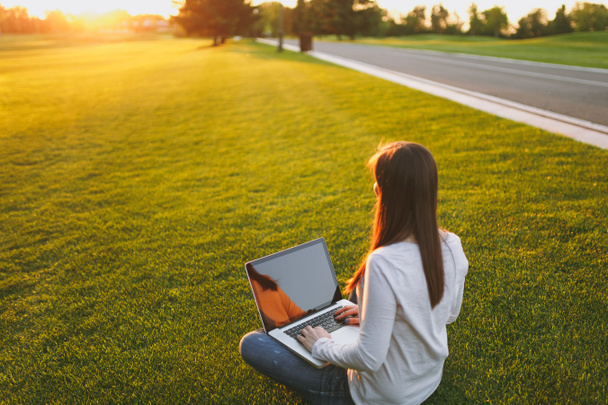 Nuori nainen näkymä taakse. Nainen työskentelee kannettavan tietokoneen tietokoneen tyhjä musta tyhjä näyttö kopioida tilaa kaupungin puistossa vihreä ruoho auringonpaiste nurmikko ulkona. Liikkuva toimisto. Freelance-liiketoiminnan käsite
 - Valokuva, kuva