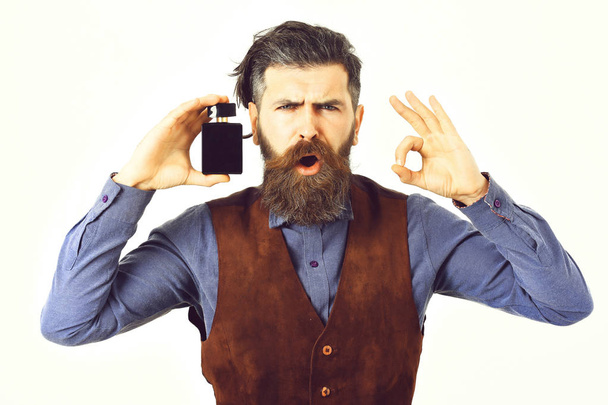 Glamur man hair style. bearded man holding perfume with surprised face - Foto, afbeelding