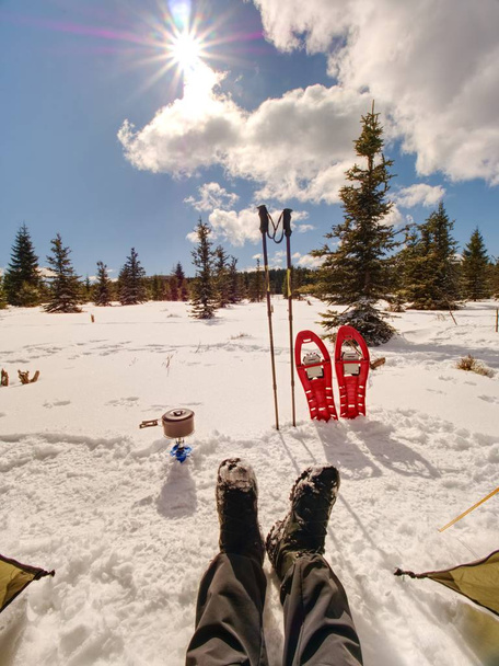 Lunchtijd tijdens de winter trail. Kamperen op sneeuw en koken. Rode sneeuwschoenen en trekking palen staan in de sneeuw. Winter mountaiins. - Foto, afbeelding