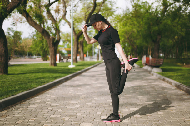 Genç atletik güzel esmer kız siyah üniforma, Cap çalışan veya şehir park açık havada duran eğitim, önce ısınma spor germe egzersizleri, yapıyor. Fitness, sağlıklı yaşam konsepti - Fotoğraf, Görsel