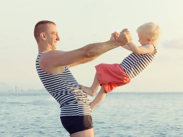Papá sostiene a su hijo en manos extendidas en la costa. Diviértete
 - Foto, Imagen
