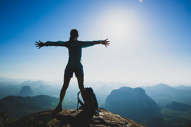 Successful cheering young woman hiker with outstretched arms on mountain peak during sunrise  - Photo, image