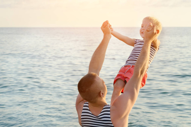 Tata trzyma jego syna w wyciągniętej ręce na morzu. Baw się dobrze - Zdjęcie, obraz