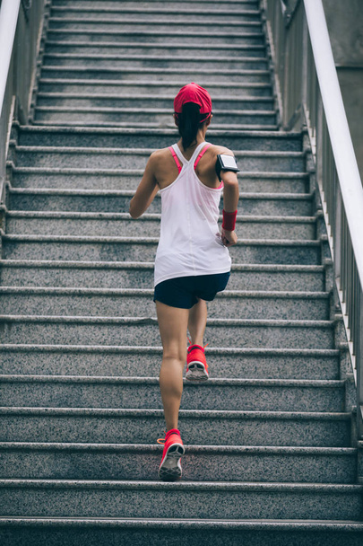 Young woman runner sportswoman climbing up city stairs jogging and running in urban training workout - 写真・画像