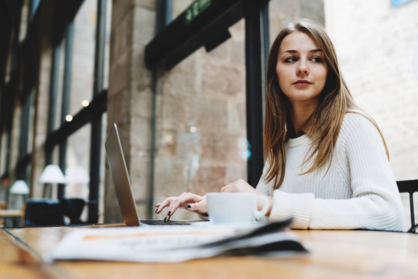 Piękna młoda kobieta za pomocą laptopa siedząc w kawiarni z laptopa i rano gazety - Zdjęcie, obraz