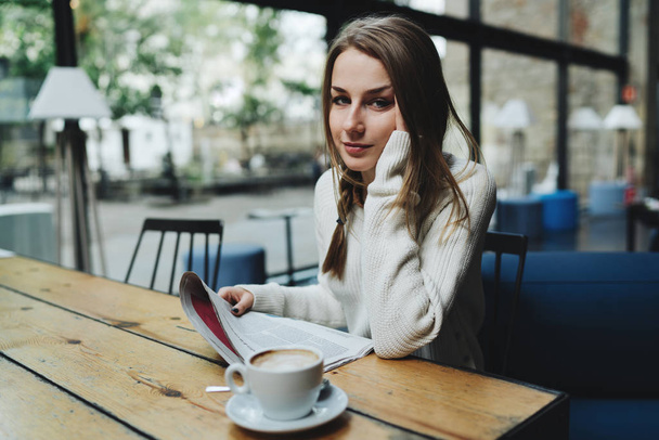 Portrait of young woman looking at the camera while holding morning business newspaper and enjoying coffee - Foto, Imagen