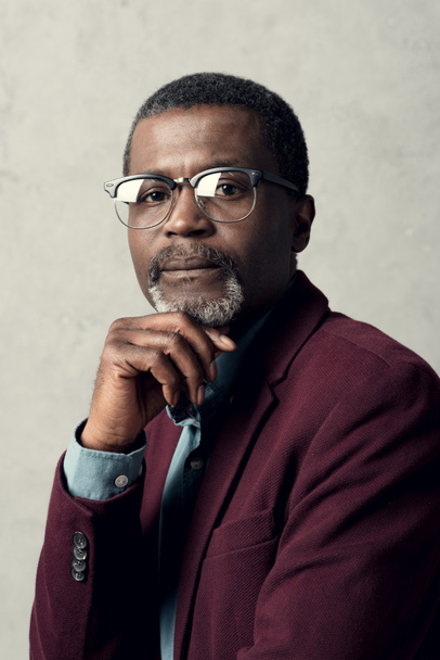 portrait of pensive african american man in trendy eyeglasses and burgundy jacket - Foto, Imagem