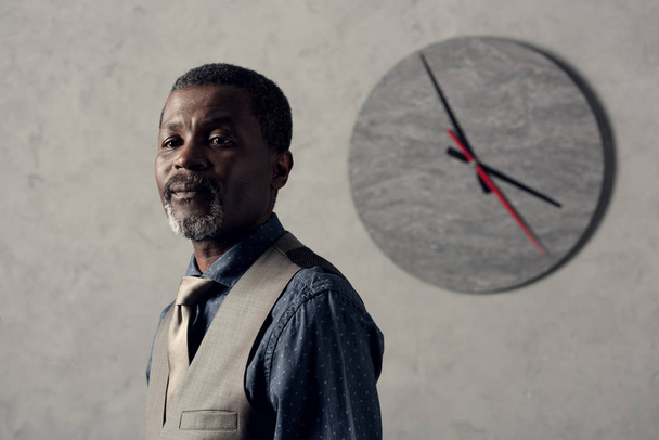portrait of stylish african american man in waistcoat with clock on wall - Fotografie, Obrázek