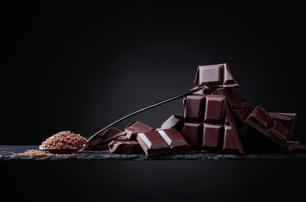 Broken black chocolate pieces and chocolate chip in small spoon on black  background. Copy space. - Photo, Image