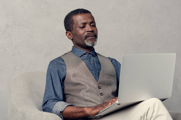 kypsä tyylikäs afrikkalainen amerikkalainen liikemies, joka käyttää kannettavaa tietokonetta töissä
 - Valokuva, kuva