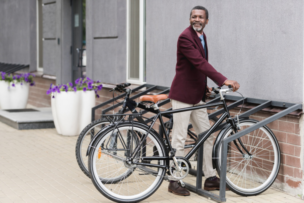 trendy african american businessman with bike on parking for bicycles - Zdjęcie, obraz