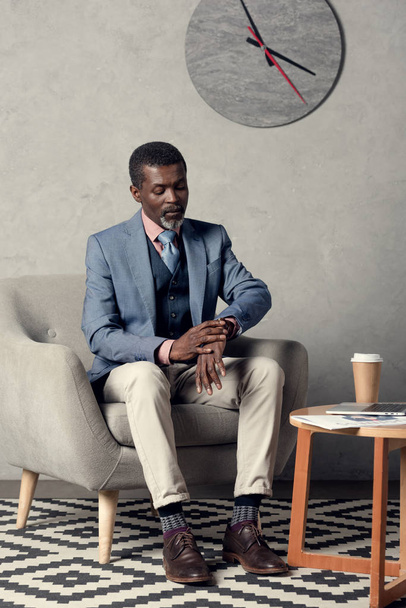 腕時計をコーヒー テーブルに座って見てスタイリッシュなアフリカ系アメリカ人のビジネスマン  - 写真・画像