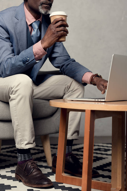 cropped view of african american man with coffee to go using laptop - Φωτογραφία, εικόνα