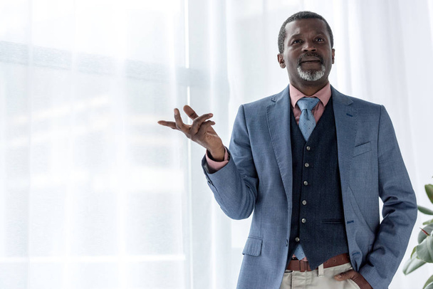 thoughtful african american businessman in blue jacket gesturing near window - Photo, Image