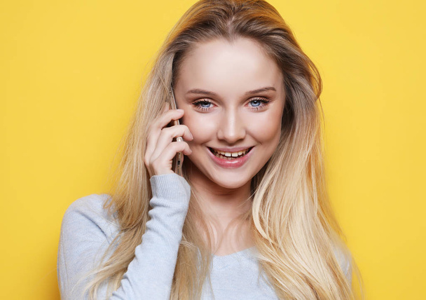 portrait of young, happy woman talking on phone looking at camera, over yellow background - Photo, image