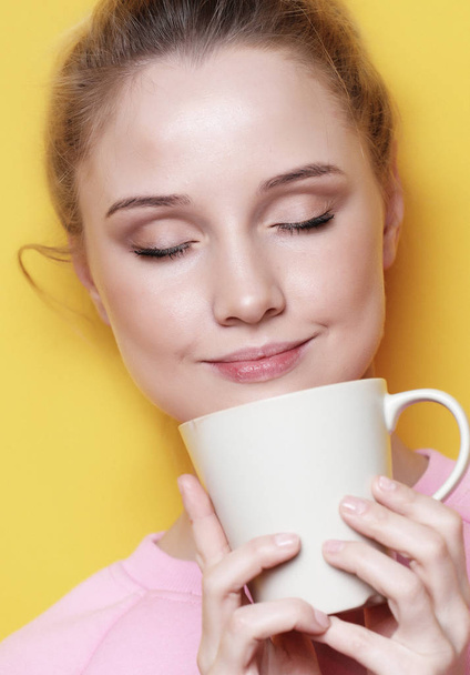 Young blond woman holding white cup with tea or coffee, lifestyle and food concept. - 写真・画像
