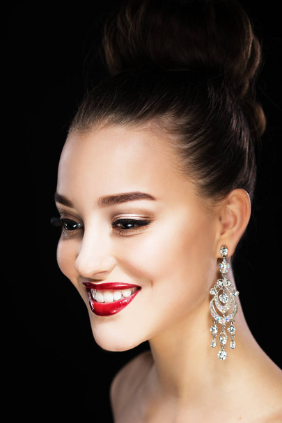Belle femme brune avec maquillage lumineux et boucles d'oreilles bijoux souriant gros plan. Lèvres et ongles rouges, maquillage du soir
 - Photo, image