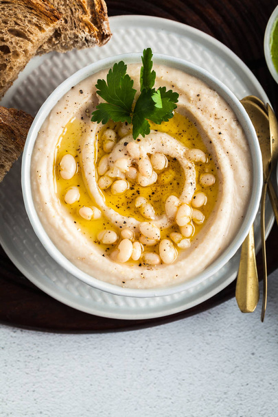 hummus of white cannellini beans, served with arugula pesto and rye bread, olives and lemon on a table - Fotó, kép