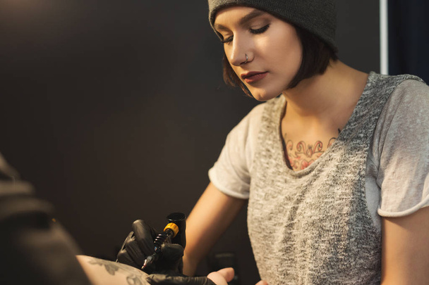 Mujer joven tatuadora haciendo tatuaje en brazo masculino
 - Foto, imagen