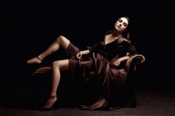 Kahverengi elbiseli kız. Stüdyoda bir kanepede oturuyor. Siyah arka plan. - Fotoğraf, Görsel