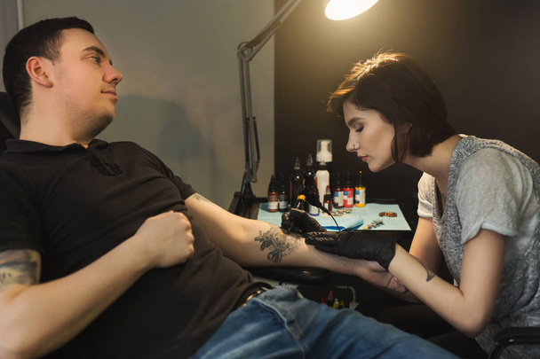 Giovane donna tatuatrice che fa tatuaggio sul braccio maschile
 - Foto, immagini