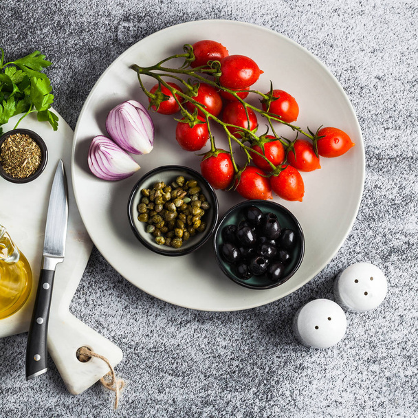 Μεσογειακή σαλάτα συστατικά σε ένα πιάτο σε ένα πέτρινο τραπέζι. Κόκκινο κρεμμύδι, ελιές, κάπαρη και τοματίνια με το ελαιόλαδο. Υγιεινά τρόφιμα - Φωτογραφία, εικόνα