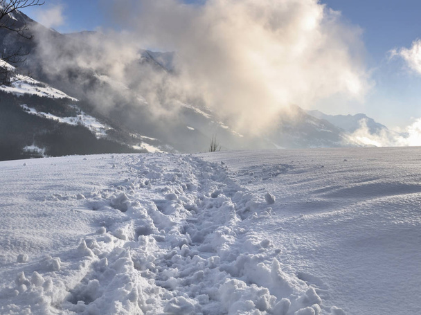 пішохідна стежка на снігу в горах з хмарами, освітленими сонцем
 - Фото, зображення