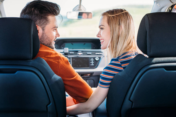 улыбающаяся молодая пара смотрит друг на друга и сидит в машине
 - Фото, изображение